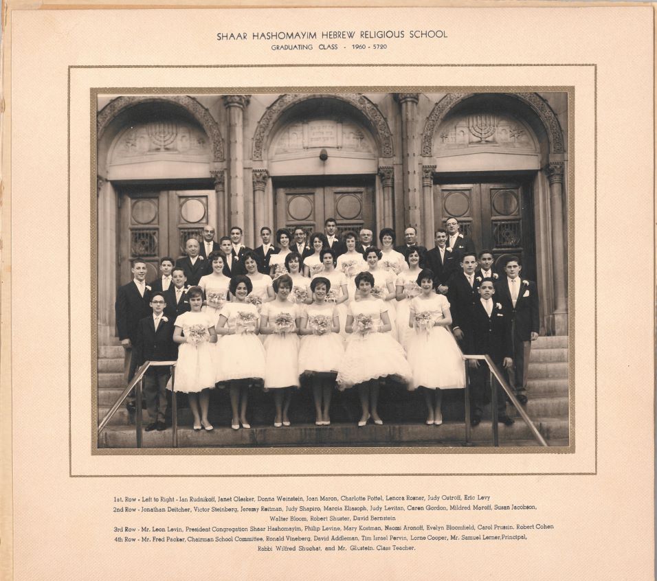 A black-and-white photograph of a group of adolescents dressed in formal attire, standing in front of a building for a school graduation.