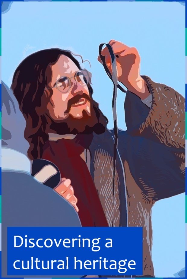 A photograph, edited to look like a comic strip, of a man with a beard and long brown hair. He is wearing a coat, a burgundy scarf, and small round glasses. He is examining a roll of film. On the lower left corner are the words: “Discovering a cultural heritage”.