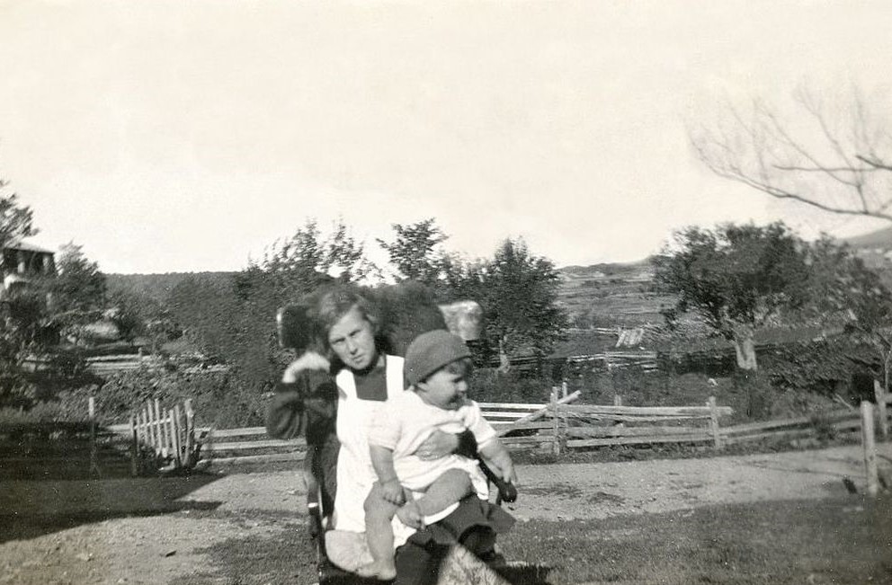A teenage girl with a baby on her lap in front of a domestic orchard