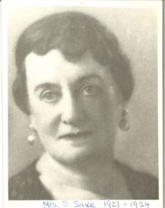 A black-and-white photograph of a middle-aged woman with pulled back hair and earrings.