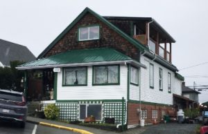 Colour photograph of a gabled two story private house with a prominent dormer window and balcony attic development situated on a sloping lot.