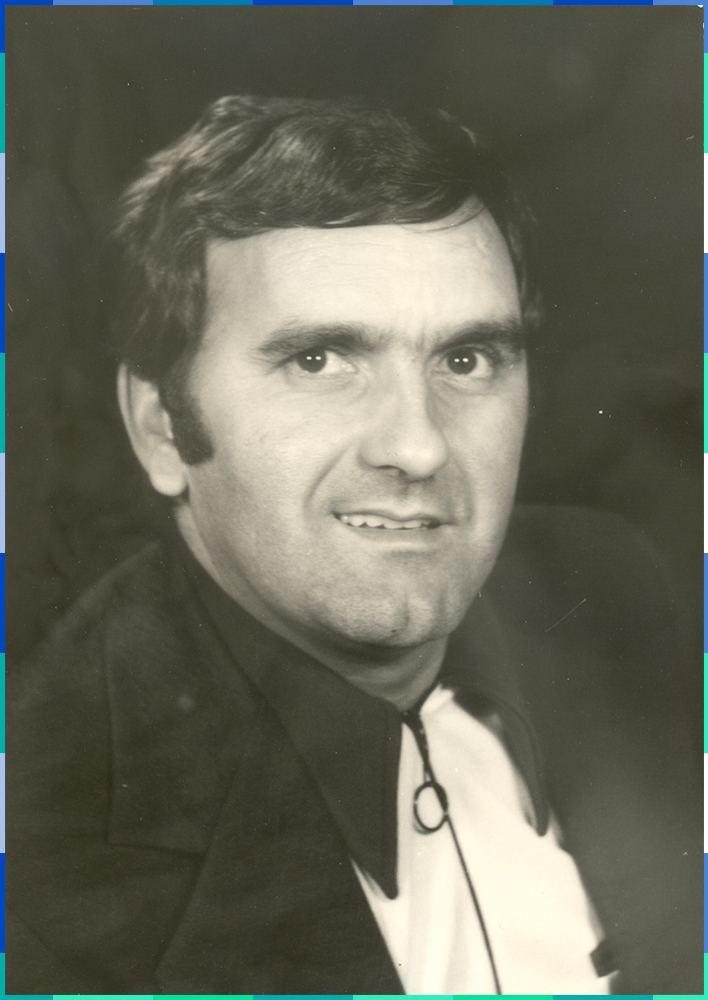 A black and white portrait of a man with short hair and thick eyebrows. There is a hint of a smile on his face.