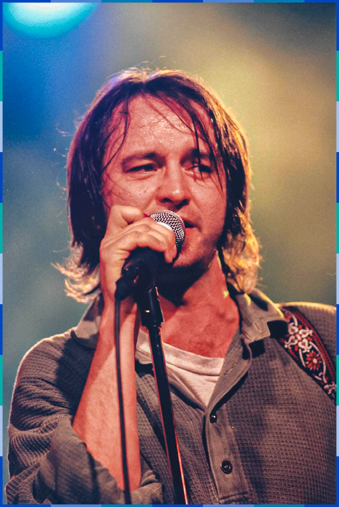 A photo of the singer Dédé Fortin on a stage, holding a microphone.