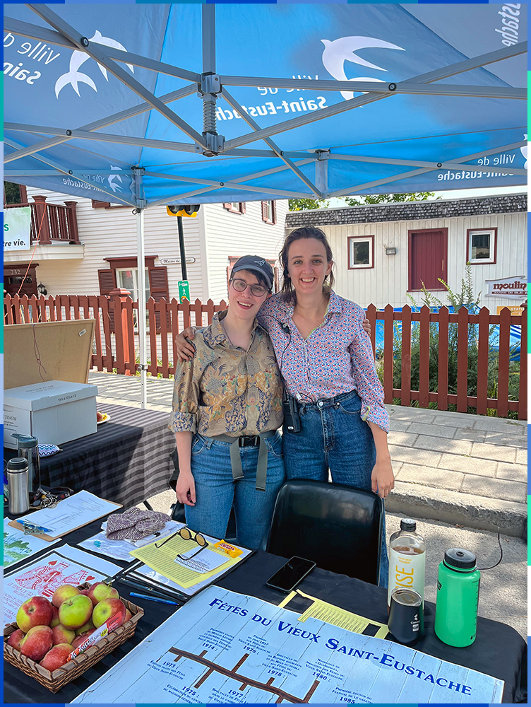 Two women under a big tent behind an outdoor table.