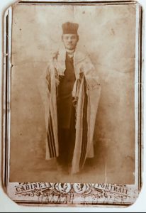 A black-and-white photograph of a man wearing cantorial robes and a prayer shawl.
