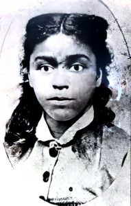 Black and white grainy oval portrait photograph of a young black woman with prominent eyes and long black curly hair parted in the middle swept back off her face.