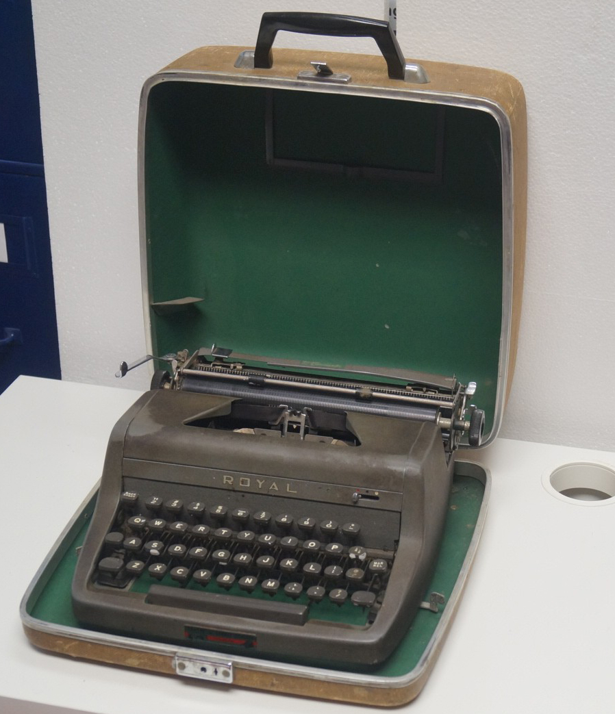 A dark grey Royal brand typewriter sitting in an opened brown carrying case lined in green.