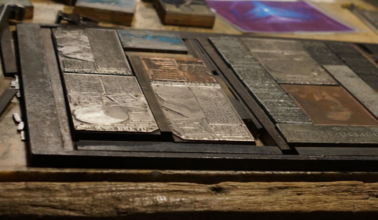 A wooden case holds flat, rectangular metal blocks of type, as well as illustrations used to print an edition of The Fisherman's Advocate newspaper, Port Union, Newfoundland.