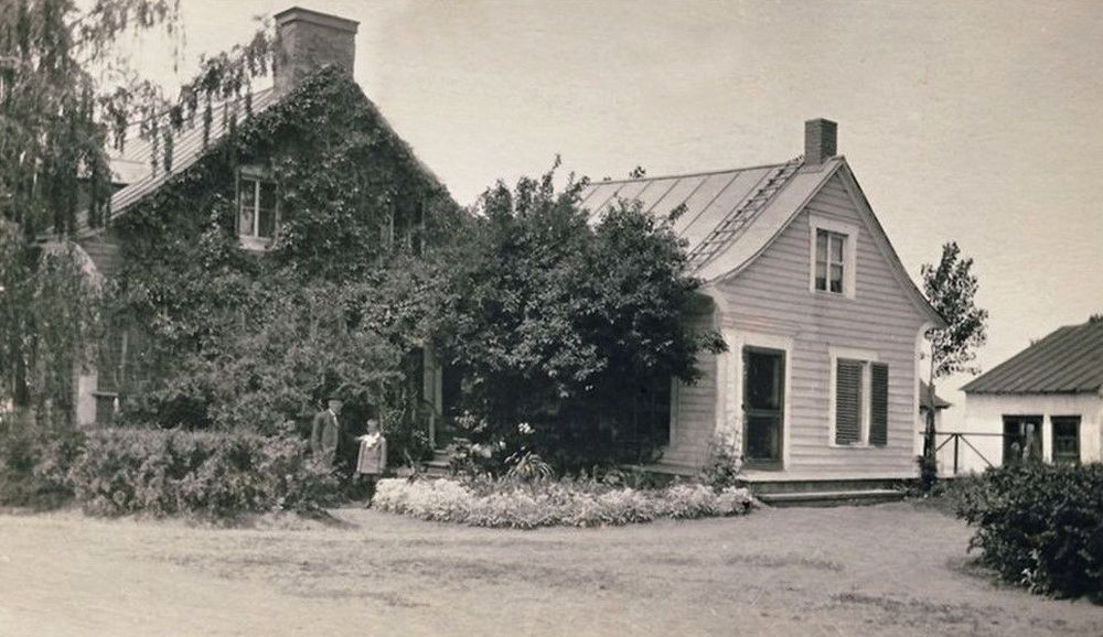 An adult and a child in front of a house covered in vines near an annex and a shed