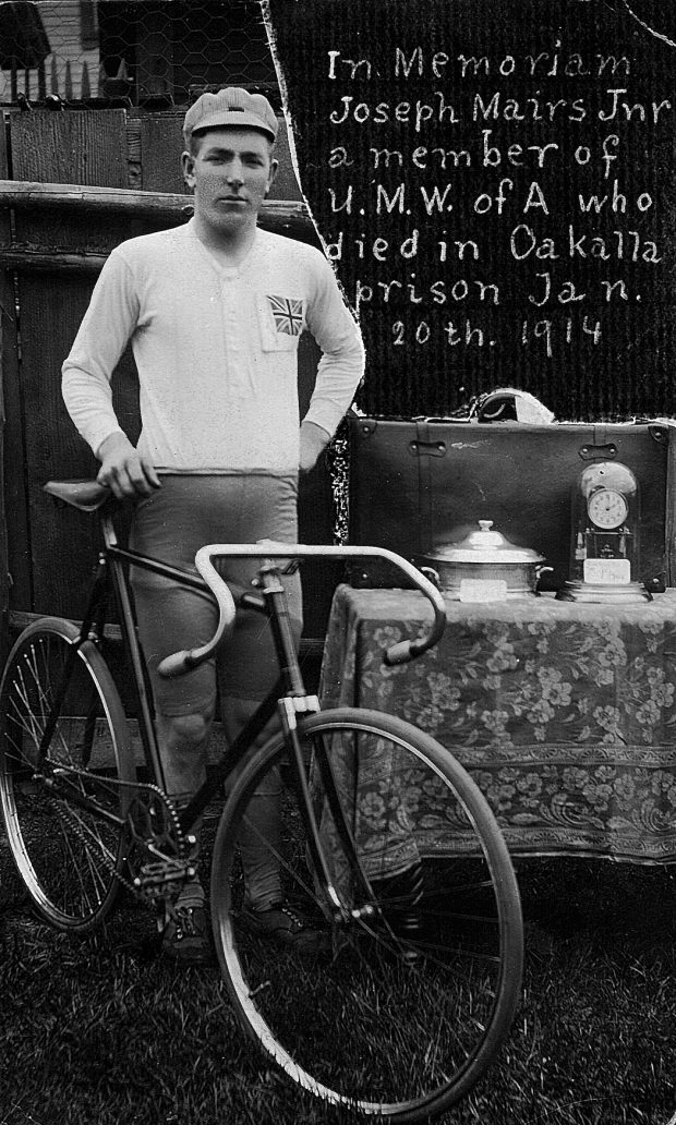 Black and white photo showing a young man standing next to an early 1900s racing bicycle.