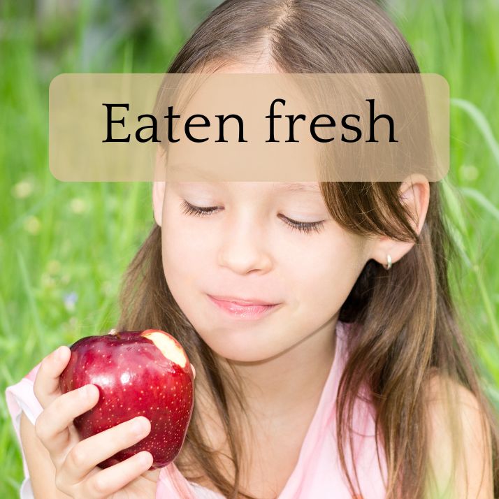 A little girl looks at an apple she has bitten into.