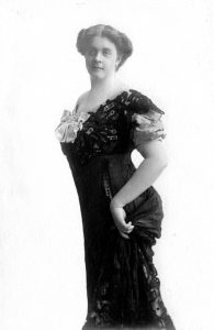 Black and white portrait photograph of a woman in a short-sleeved early 20th-century opera gown.
