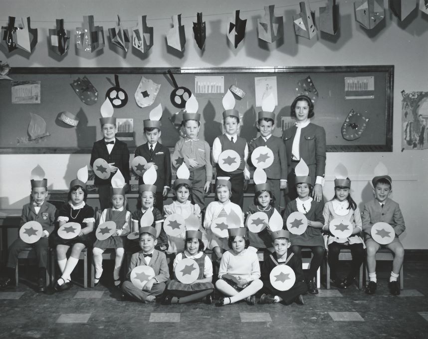 A black-and-white photograph of a group of children in a classroom celebrating Chanukah.