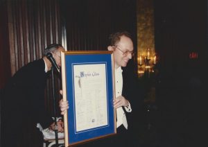 Music Director Stephen Glass holding a large certificate.
