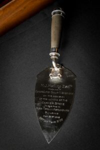 A close-up of a silver trowel, engraved with text.