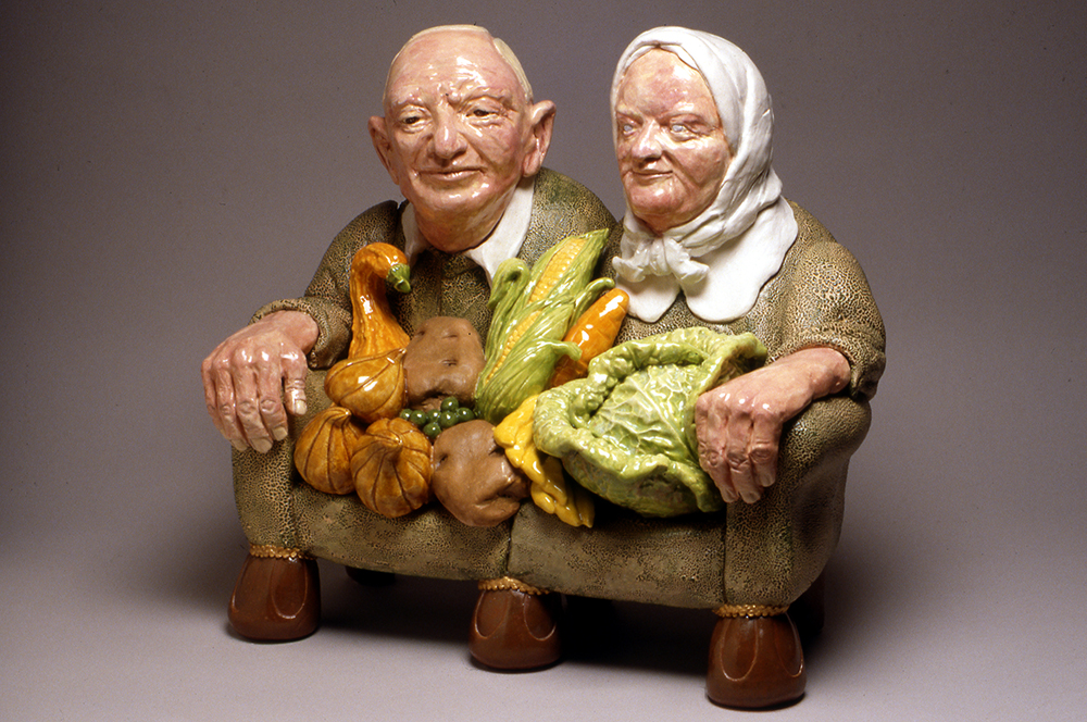 Ceramic sculpture of an elderly couple merged with a couch and holding vegetables