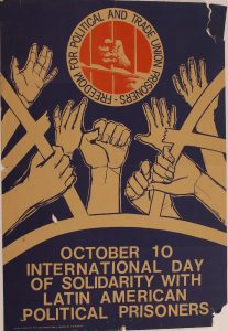 This poster has a blue background with white text that states October 10 International Day of Solidarity With Latin American Political Prisoners at the bottom of the page. Above the text is a graphic of a group of arms tearing open a cage. Above this image is an orange logo in the shape of a circle of a hand grasping a prison bar. Encircling the image is the text Freedom For Political And Trade Union Prisoners.