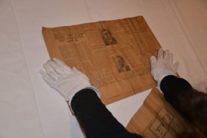 An old Yiddish newspaper laid out on a table, being flattened by a person wearing white gloves.
