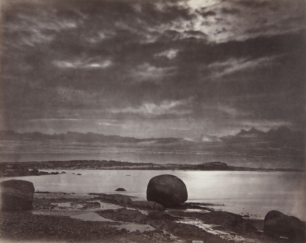 Albumen print (1876, Alexander Henderson): Evening on the beach at Métis (melancholy twilight seascape). Dominant sky (dark textured clouds, openings of light). Foreground: wet rocky beach (large dark rocks including a rounded block in the centre right).