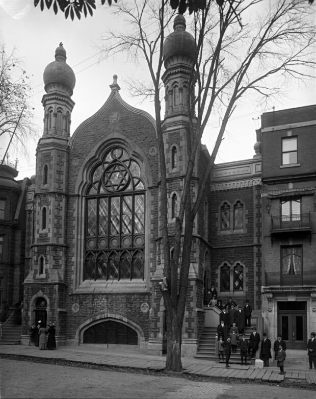 A black-and-white photograph of the exterior of a synagogue built in the Moorish Revival. a group of people gathers on the synagogue's stairs.