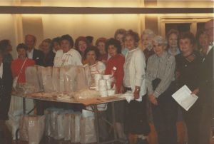 A group of women from the synagogue's sisterhood standing around a table with meals for delivery.