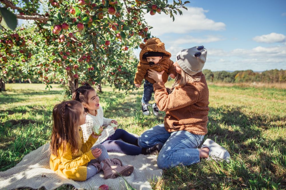 A mother and three children are picnicking in an orchard