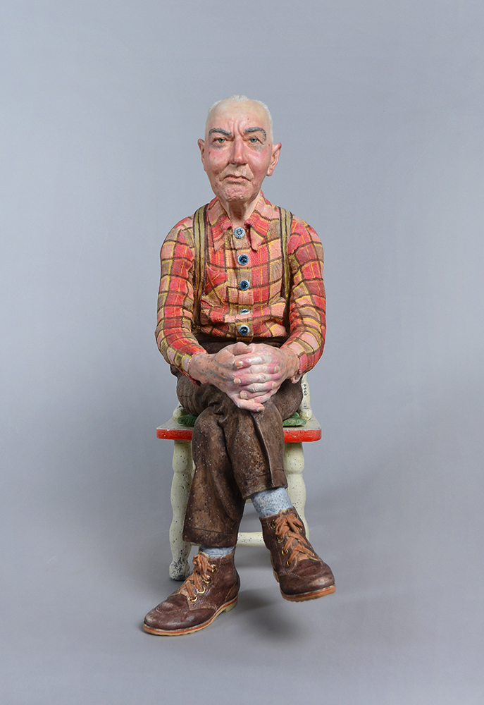 Sculpture of seated man in red and orange plaid shirt and brown pants.