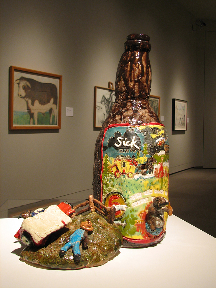 Clay sculpture of a large beer bottle and next to it a smaller farmer asleep in a field.