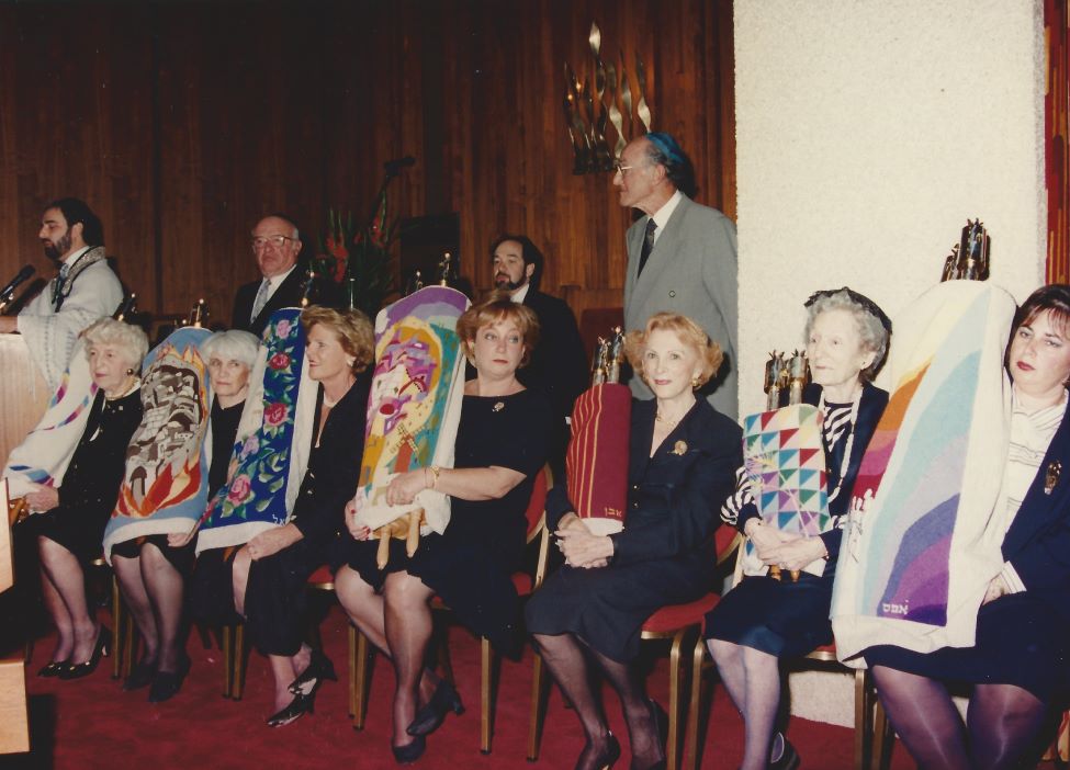 A group of women sitting in chairs, holding Torah scrolls.