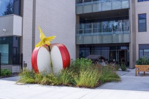 Sculpture: a hummingbird on a giant apple in front of a building