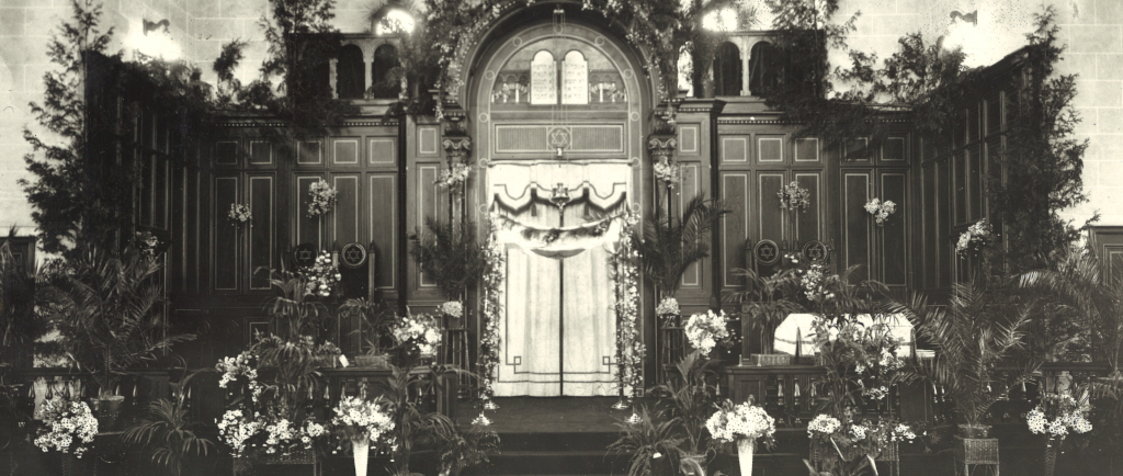A black-and-white photograph of a synagogue interior, decorated for a wedding.